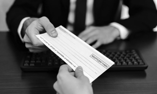 Two people exchanging a returned cheque across an office desk, in black and white